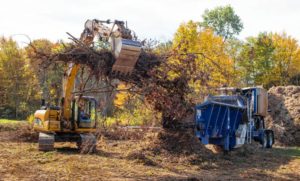 An excavator puts tree branches and brush into a mulcher as they clear out the river bank of Suncook on October 10, 2017. GEOFF FORESTER/Monitor staff