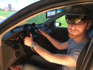In UNH’s driving simulator, a researcher wears Microsoft HoloLens augmented reality glasses, which overlay virtual objects on the “world” shown by the simulator. Photo by Andrew Kun/UNH