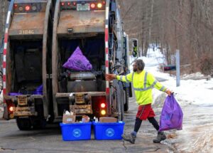 el Duclos of Casella Waste Systems tosses in a purple bag as he holds another on the pickup route on Elm Street in Penacook on Thursday morning. GEOFF FORESTER