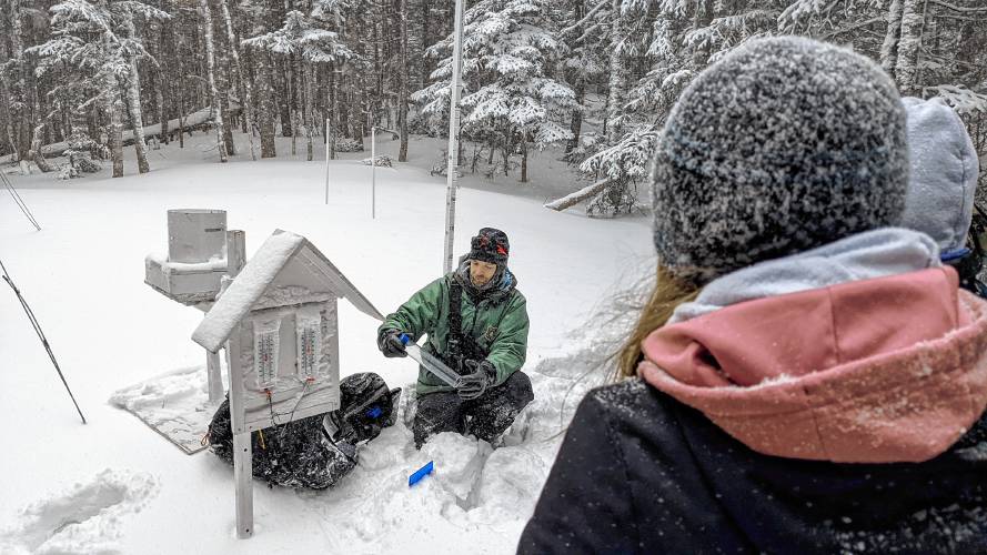 Mount Washington Avalanche Center forecaster demonstrates to students how to use a snow tube to measure the weight and density of new snow, alongside a weather station, during the winter of 2021-22. USDA Forest Service