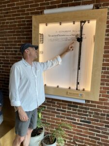 Richard Stoyle describes the workings of his wall-mounted printer in Revelstoke Coffee, which is drawing a copy of the Declaration of Independence. The drawing will probably be finished on Saturday, July 5.